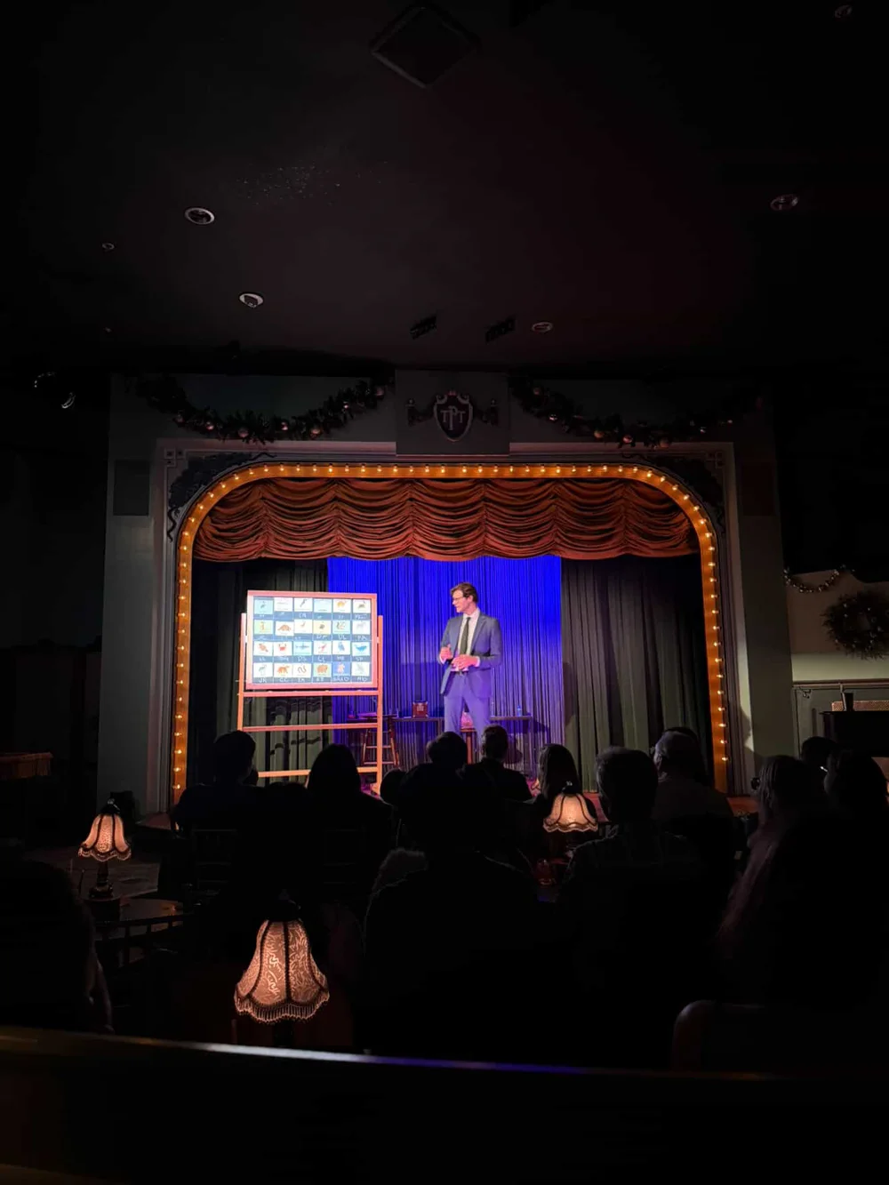 Kevin performing on the illuminated Palace stage, seen across the seated audience
